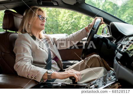 Businesswoman sitting by open window in car and driving to office for meeting 68528517