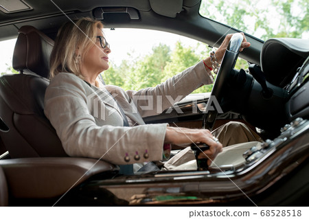 Side view of mature woman sitting by open window in car and driving to work Side view of mature woman sitting by open window in car and driving to work 68528518