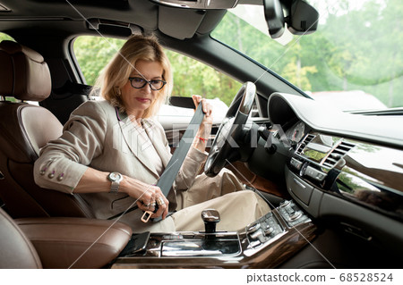 Contemporary mature businesswoman fastening seatbelt before driving to work 68528524