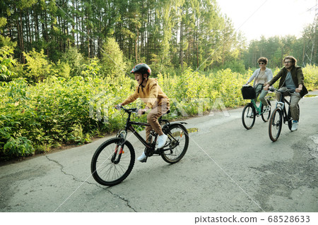 Young couple and their son riding bicycles along road in natural environment Young couple and their son riding bicycles along road in natural environment 68528633