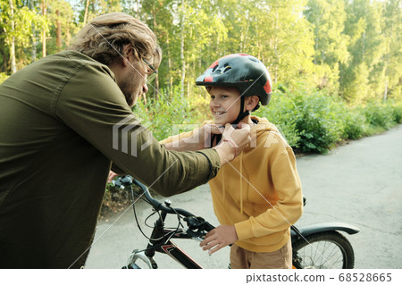 Young man in eyeglasses and casualwear helping his youthful son to tie up belts Young man in eyeglasses and casualwear helping his youthful son to tie up belts 68528665