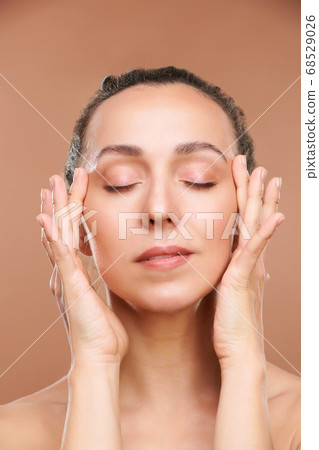Pretty female with closed eyes touching eyelids while taking care of her face 68529026