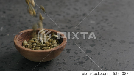 dried pumpkin seeds falling into olive bowl on terrazzo countertop 68530881