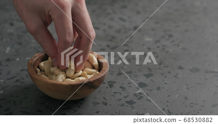 man hand takes cashew nuts from olive bowl on terrazzo countertop man hand takes cashew nuts from olive bowl on terrazzo countertop 68530882