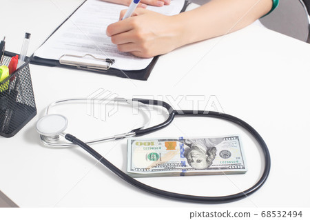 A stethoscope and money dollars lie on a white medical table at the doctor's. Concept of bribery in medicine and sale of clandestine drugs, copy space 68532494