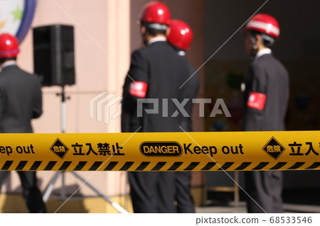 參加防災演練的人員在控制線上排隊和黃色膠帶 參加防災演練的人員在控制線上排隊和黃色膠帶 68533546