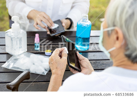 Cleaning mobile phone to eliminate germs,Covid-19,asian women cleaning the phone by hand sanitizer gel,elderly people using alcohol to wipe to avoid contamination,disinfection,outbreak of Coronavirus 68533686