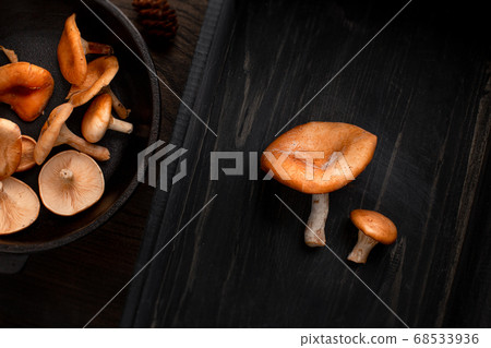Raw fresh mushroomon on cast-iron pan left, and two mushrooms on right, on wood background. Top view, space for text 68533936