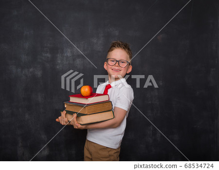 Adorable child whit books and apple in hands. Back to school. Education. Blackboard on background. Kid pupil boy in uniform. 68534724