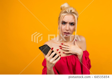 dissatisfied girl in a red dress with a phone in her hands on a yellow background with copy space dissatisfied girl in a red dress with a phone in her hands on a yellow background with copy space 68535854