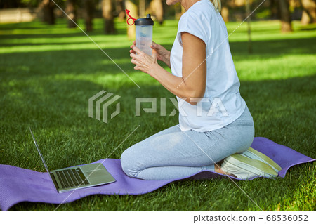 Sporty woman drinking water and using laptop in park 68536052