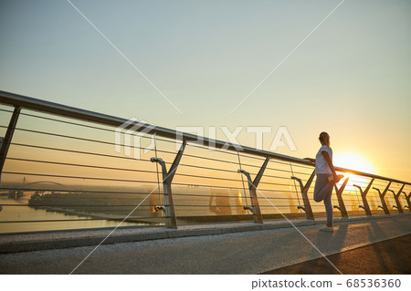 Sporty woman stretching legs on the bridge Sporty woman stretching legs on the bridge 68536360