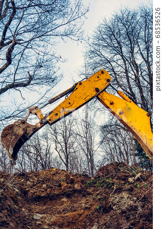 A yellow excavator in the forest digs a pit for a A yellow excavator in the forest digs a pit for a 68536526