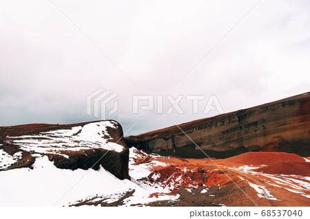 Martian landscapes in Iceland. The red crater of The Seydisholar volcano. The quarry of red soil mining. White snow lies on red soil. Martian landscapes in Iceland. The red crater of The Seydisholar volcano. The quarry of red soil mining. White snow lies on red soil. 68537040
