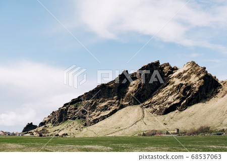 A green meadow, a field for grazing cattle with grass, against the backdrop of rocky mountains and blue sky with white clouds in Iceland. A green meadow, a field for grazing cattle with grass, against the backdrop of rocky mountains and blue sky with white clouds in Iceland. 68537063