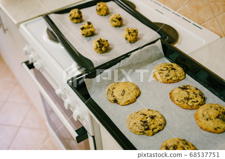 Two baking trays on the kitchen table - with cooked American cookies and raw dough balls. Two baking trays on the kitchen table - with cooked American cookies and raw dough balls. 68537751