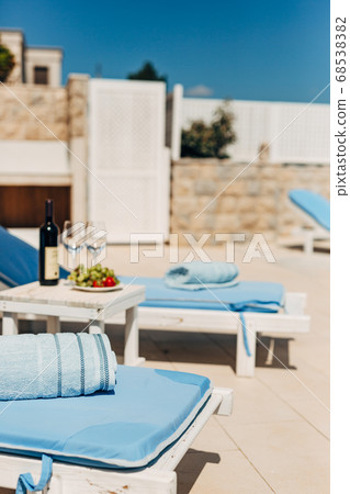 Blue towels on sun loungers on the beach. Table with wine, glasses and grapes. Blue towels on sun loungers on the beach. Table with wine, glasses and grapes. 68538382
