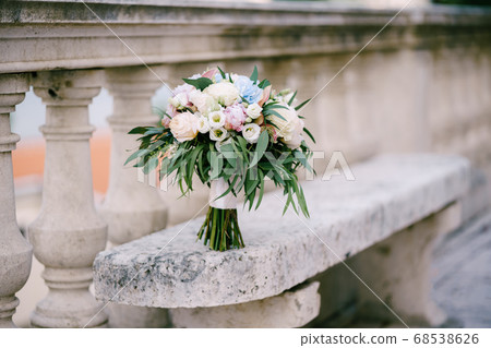 bridal bouquet of white and pink roses, peonies, hortense branches of eucalypt tree, eustoma and white ribbons on the stone bench near railing of an ancient staircase bridal bouquet of white and pink roses, peonies, hortense branches of eucalypt tree, eustoma and white ribbons on the stone bench near railing of an ancient staircase 68538626
