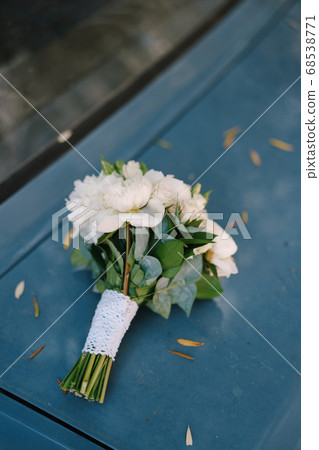 bridal bouquet of white peonies, roses, branches of eucalypt tree and lace ribbon on the hood of the car bridal bouquet of white peonies, roses, branches of eucalypt tree and lace ribbon on the hood of the car 68538771