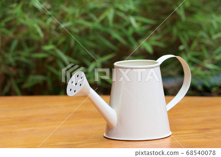 Small white watering can on the wooden floor. 68540078