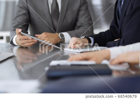 Unknown businessman using tablet computer and working together with his colleague while sits at the glass desk in modern office. Teamwork and partnership concept 68540679