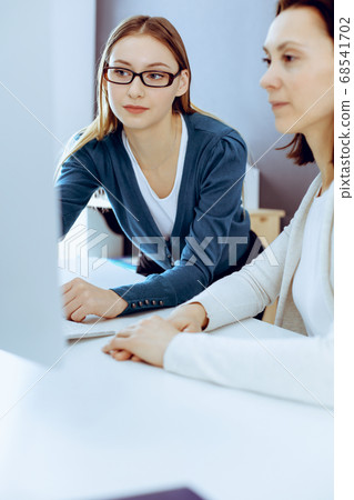Businesswoman giving presentation to her female colleague while they sitting at the desk with computer. Group of business people working in office. Teamwork concept Businesswoman giving presentation to her female colleague while they sitting at the desk with computer. Group of business people working in office. Teamwork concept 68541702
