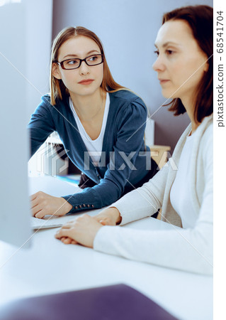 Businesswoman giving presentation to her female colleague while they sitting at the desk with computer. Group of business people working in office. Teamwork concept Businesswoman giving presentation to her female colleague while they sitting at the desk with computer. Group of business people working in office. Teamwork concept 68541704