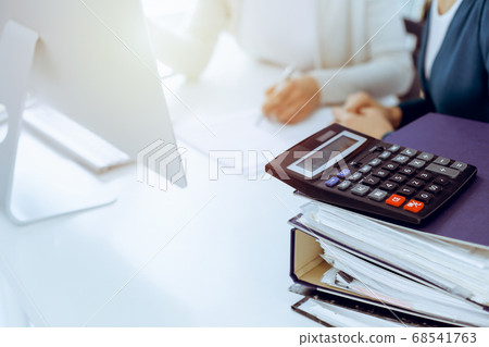 Calculator and binders with papers are waiting to be processed by business woman or bookkeeper working at the desk in office back in blur. Internal Audit and tax concept Calculator and binders with papers are waiting to be processed by business woman or bookkeeper working at the desk in office back in blur. Internal Audit and tax concept 68541763