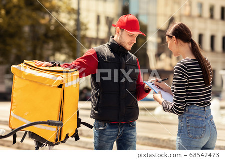 Customer Girl Signing Papers Standing With Delivery Guy Outdoors Customer Girl Signing Papers Standing With Delivery Guy Outdoors 68542473