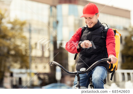 Happy Courier Checking Time On Wristwatch Sitting On Bike Outdoor Happy Courier Checking Time On Wristwatch Sitting On Bike Outdoor 68542603