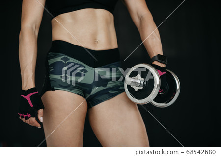 Slim muscular belly of fitness model. Athletic young woman doing fitness workout with dumbbells Slim muscular belly of fitness model. Athletic young woman doing fitness workout with dumbbells 68542680