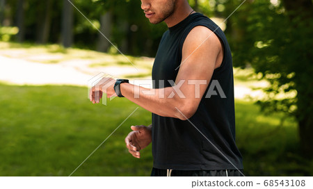 Unrecognizable black sportsman checking his smartwatch during his run at park, empty space 68543108