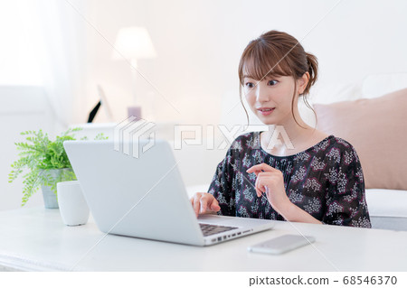 Young woman drinking tea while talking with friends on zoom in living room Young woman drinking tea while talking with friends on zoom in living room 68546370