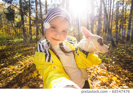 Little girl taking selfie with her dog at autumn park. Child posing with jack russell terrier for a picture on the mobile phone outdoors. Pet and children concept. 68547476
