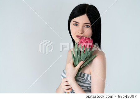 Portrait of a beautiful girl with dark hair and natural makeup with a protea flower in her hands. 68549397