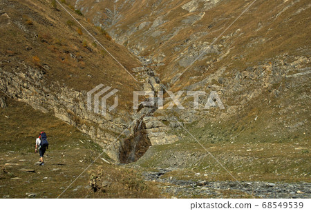 Young man with little child in baby backpack hiking in mountains. Background of rocky valley and hills at autumn time Young man with little child in baby backpack hiking in mountains. Background of rocky valley and hills at autumn time 68549539