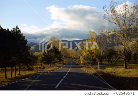 Beautiful autumn view of road among hills and colorful trees with yellow golden leaves on background of mountains 68549571