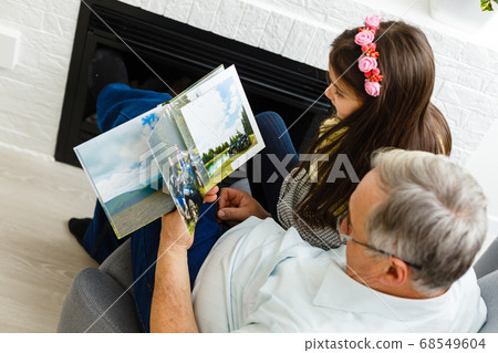 Granddaughter and grandfather watching photos together in a photo album at home Granddaughter and grandfather watching photos together in a photo album at home 68549604