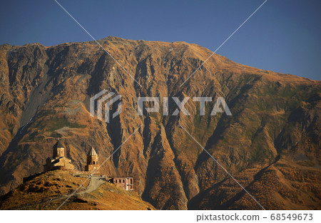 Beautiful view of Gergeti Trinity Church under Mount Kazbegi. Background of autumn mountains and sky, Caucasus, Georgia Beautiful view of Gergeti Trinity Church under Mount Kazbegi. Background of autumn mountains and sky, Caucasus, Georgia 68549673