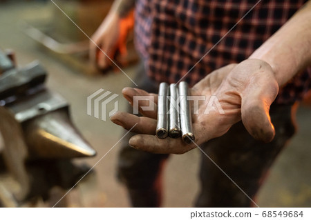Crop man showing metal tubes on blurred background of forge Crop man showing metal tubes on blurred background of forge 68549684