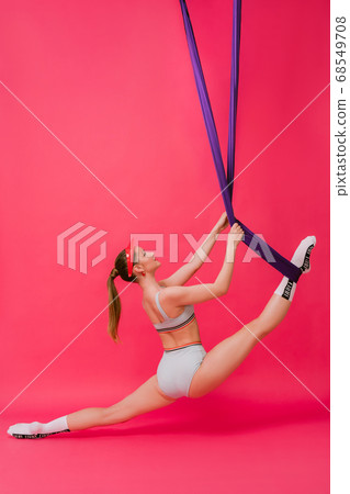 Full length body size view portrait sexy attractive strong sporty young womant gymnast in retro swimsuit hangs on air silk stretch out in split looking up isolated over pink red background Full length body size view portrait sexy attractive strong sporty young womant gymnast in retro swimsuit hangs on air silk stretch out in split looking up isolated over pink red background 68549708