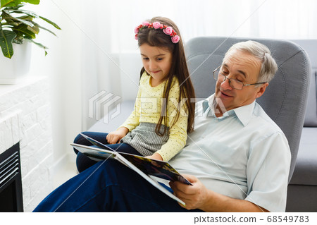 Granddaughter and grandfather watching photos together in a photo album at home Granddaughter and grandfather watching photos together in a photo album at home 68549783