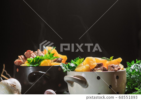 hot steamed potato stew, baked with meat pork and parsley in a deep plate next to a spice numerically carrot on a black table. copy space, close up, horizontal orientation hot steamed potato stew, baked with meat pork and parsley in a deep plate next to a spice numerically carrot on a black table. copy space, close up, horizontal orientation 68551893
