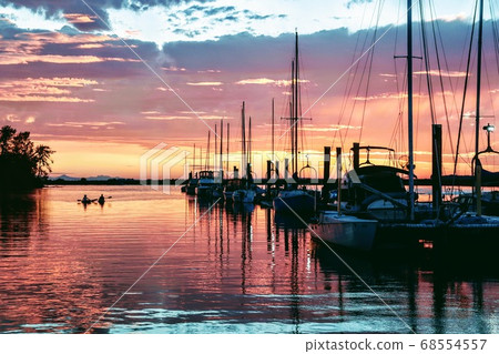 The sea and boats reflected in the red sunset of a midsummer night, and a couple's kayaking The sea and boats reflected in the red sunset of a midsummer night, and a couple's kayaking 68554557