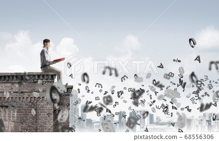 Man on roof edge reading book and symbols flying around 68556306