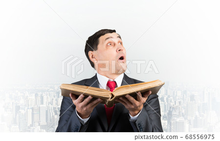 Surprised businessman holding open old book Surprised businessman holding open old book 68556975