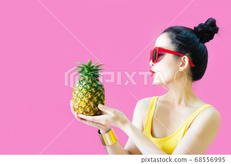 Happy beautiful asian woman in yellow undershirt,sunglasses fashion holds pineapple in her hands posing with pineapple, female funny with pineapple in summer holidays isolated on pink background 68556995