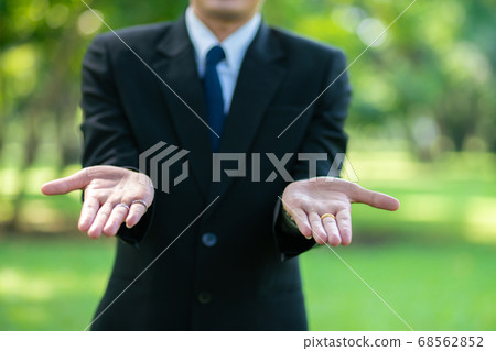 Handsome business man show blank hand in city park Handsome business man show blank hand in city park 68562852