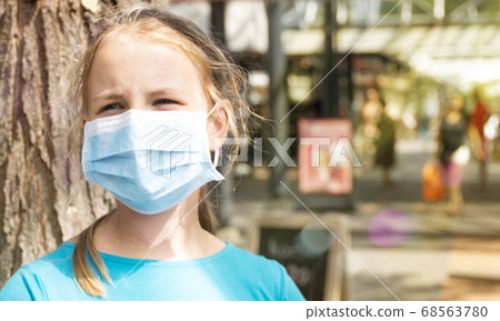 On a hot summer day sad girl wears a medical mask on the city street during quarantine. 68563780