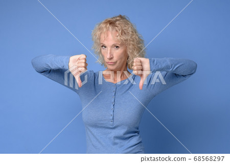 Gloomy dissatisfied mature woman looks at camera show thumbs down 68568297
